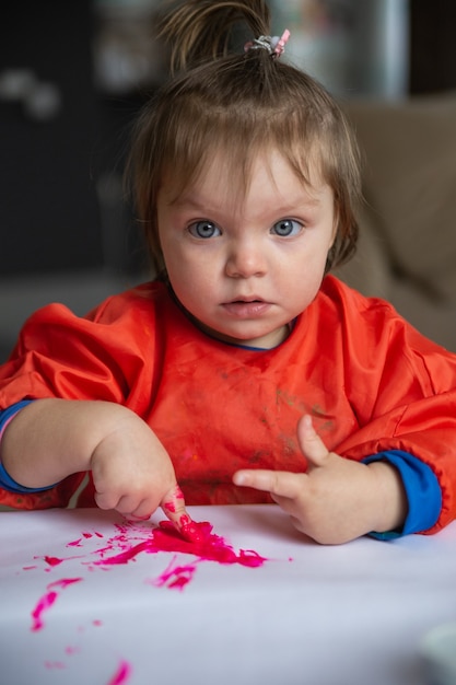 uma menina está sentada a uma mesa e desenhando com tintas a dedo. O conceito de desenvolvimento inicial