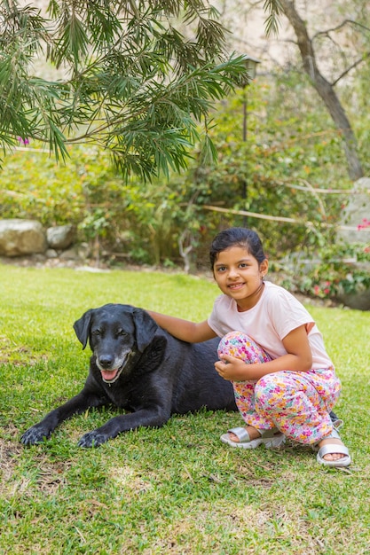 Uma menina está sentada na grama ao lado de um cão preto