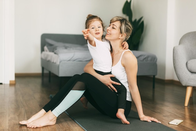 Uma menina está sentada no colo de sua mãe descansando depois de um exercício de fitness abraçando-a sorrindo
