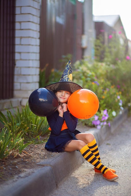 Uma menina fantasiada de bruxa e com balões para o Halloween caminha pela rua e se alegra com o feriado