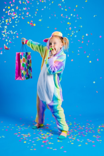 Uma menina feliz em um unicórnio kigurumi segura uma sacola de presente