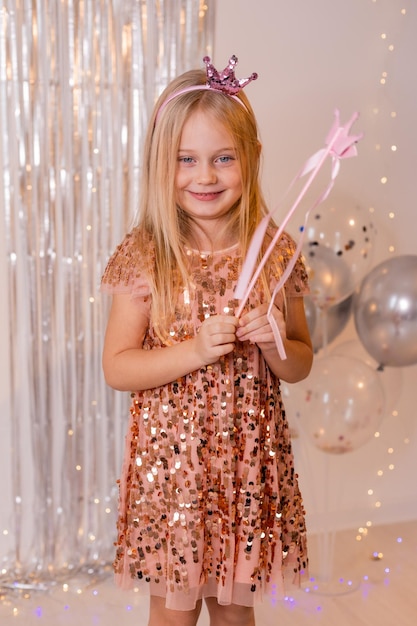 uma menina feliz em um vestido elegante e uma coroa sopra confete das palmas das mãos e faz um desejo.