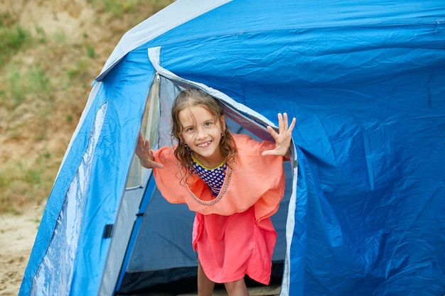 Uma menina feliz olha para fora de uma tenda à beira-mar