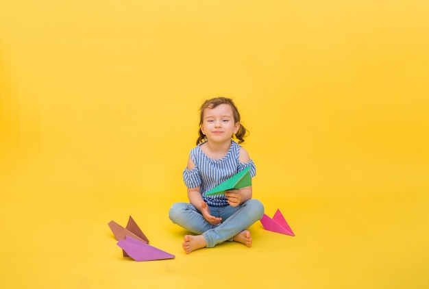 Uma menina feliz senta-se com aviões de papel origami amarelo