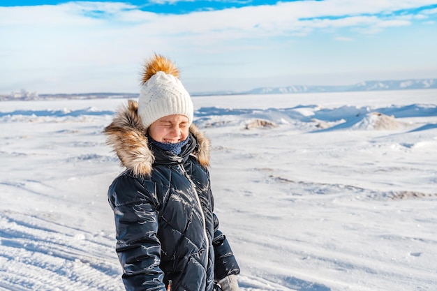 Uma menina feliz sozinha no meio de um deserto de neve em um rio congelado em um dia ensolarado de inverno