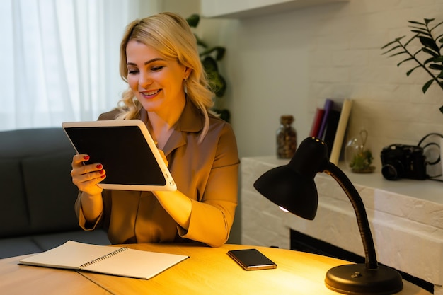 Uma menina feliz trabalha remotamente de casa e se comunica por videochamada com amigos e parentes em seu escritório. Ensino à distância e trabalho online. Usando o tablet