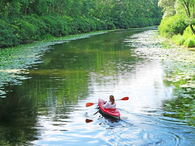 Uma menina flutua sonhadoramente seu caiaque em um rio cercado por plantas do rio Uma viagem romântica no rio sozinha Uma foto atmosférica pensativa Treino matinal na água