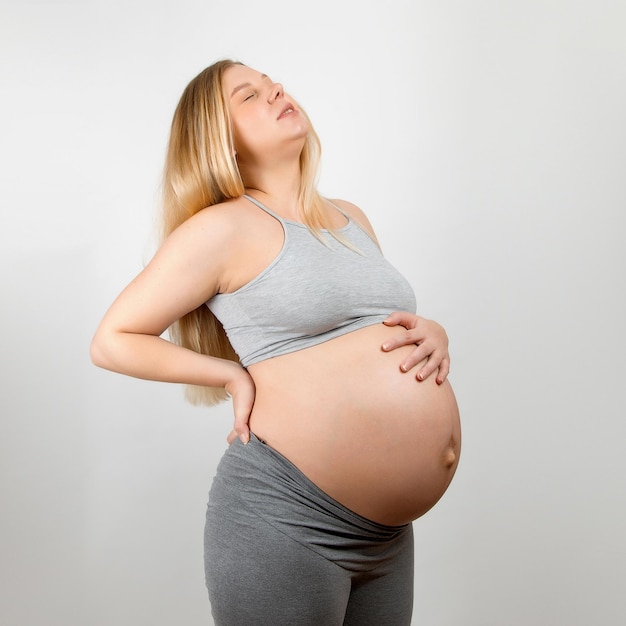 Uma menina grávida em um fundo cinza Grande dor nas costas do estômago