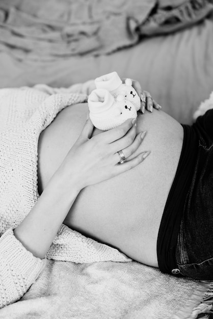 Uma menina grávida está esperando o filho desejado. há botas em sua barriga para a filha. fotografia a preto e branco