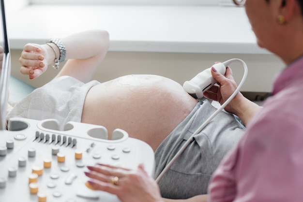 Uma menina grávida está tendo um ultra-som do abdômen na clínica em close-up. Exame médico.