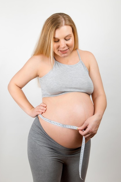 Uma menina grávida mede seu estômago com uma fita adesiva Acompanhando o progresso do crescimento do abdômen e do bebê
