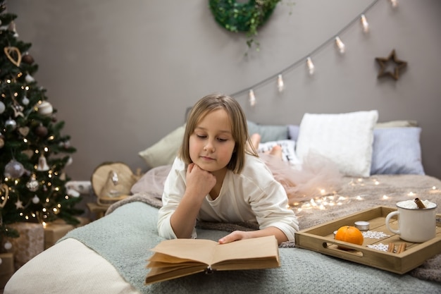 Uma menina lê um livro em uma cama no quarto