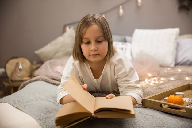 Uma menina lê um livro em uma cama no quarto