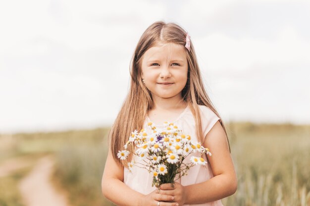 Uma menina linda com um buquê de margaridas em um campo de trigo