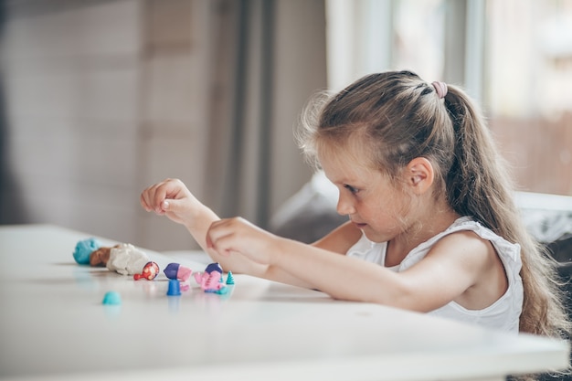 Uma menina linda em idade pré-escolar brincando de jogos educativos com bonecos de plasticina se preparando para a escola