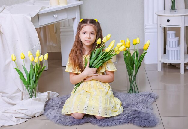 Uma menina linda em um vestido amarelo contra o fundo de buquês de tulipas amarelas