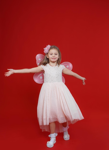 Uma menina linda em um vestido de fada fica sobre um fundo vermelho isolado.