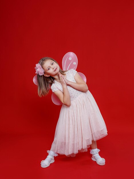 Uma menina linda em um vestido de fada fica sobre um fundo vermelho isolado.