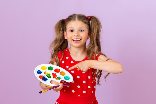 Uma menina linda em um vestido vermelho está segurando uma paleta de tinta e um pincel.