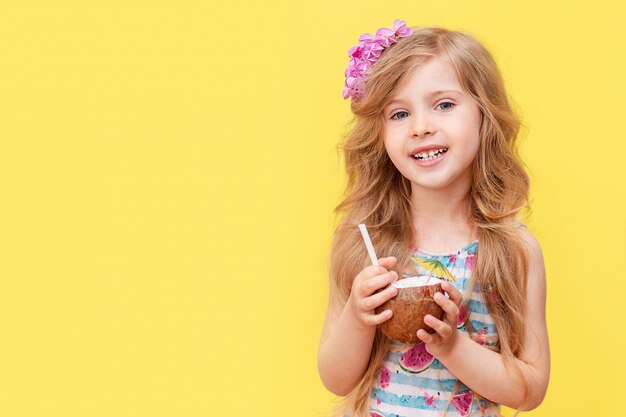 Uma menina loira alegre bebe um cocktail de coco