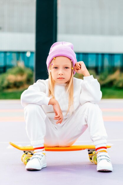 Foto uma menina loira anda de skate uma menina elegante com um chapéu senta-se em um skate e posa