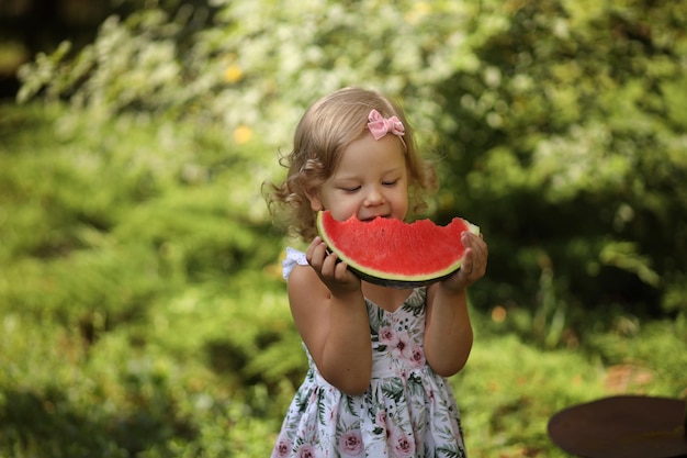 Foto uma menina loira bonitinha come uma melancia vermelha fresca no verão na rua