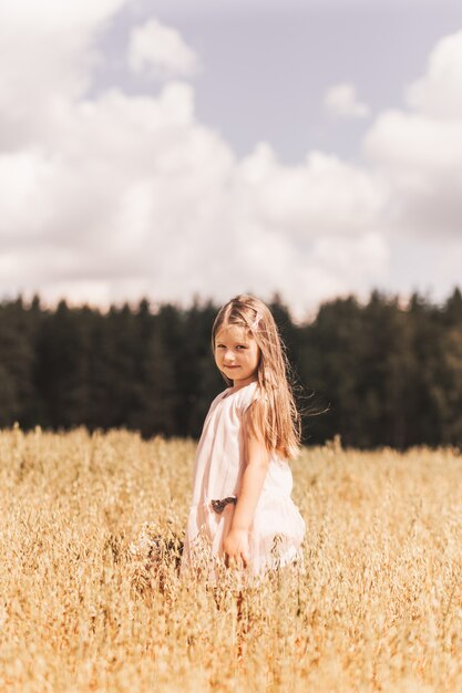 Uma menina loira caminha por um campo dourado no verão. conceito de pureza, crescimento, felicidade