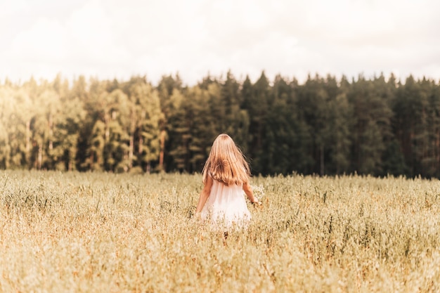 Uma menina loira caminha por um campo dourado no verão. conceito de pureza, crescimento, felicidade