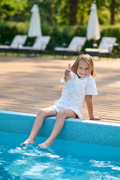 Uma menina loira sentada perto da piscina