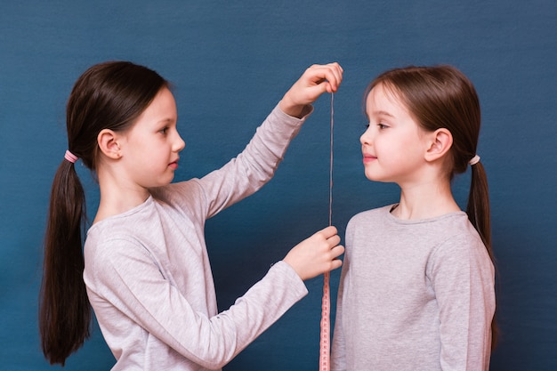 Uma menina mede outro crescimento com uma fita métrica em um fundo azul