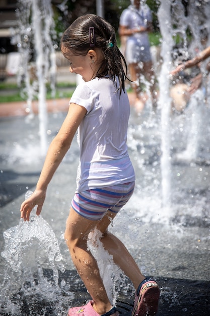 Uma menina molhada está se refrescando em uma fonte em um dia quente de verão.