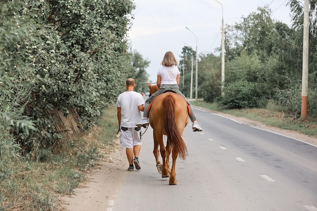 Uma menina monta um cavalo acompanhada de seu pai no quente verão