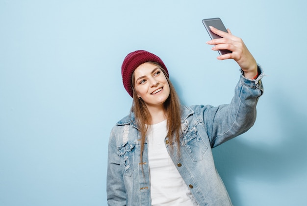 Uma menina morena com um telefone celular que se faz selfie e feliz sobre um fundo azul