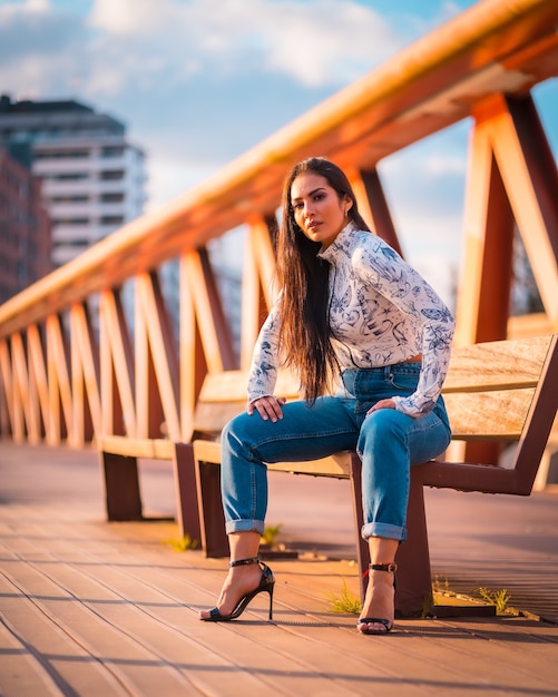 Uma menina morena latina em um jeans na cidade ao pôr do sol em um suéter laranja