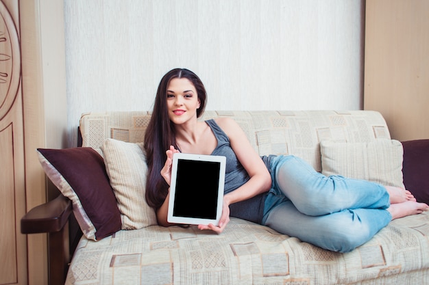 Uma menina mostra uma tela de tablet sentado em um sofá bege