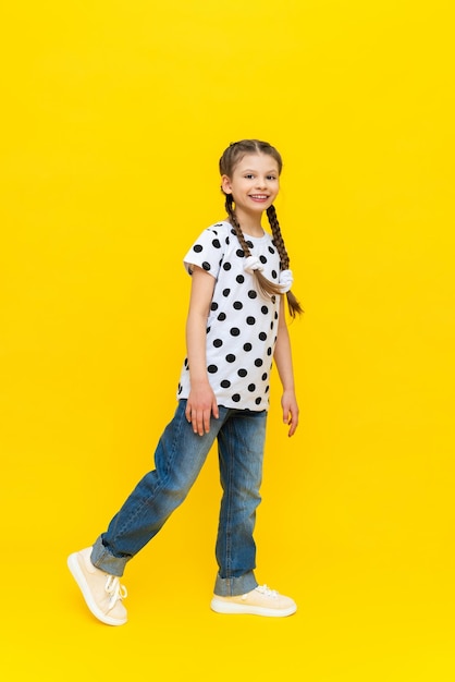 Uma menina muito bonita de jeans azul vai para a escola de uma criança em um fundo amarelo isolado