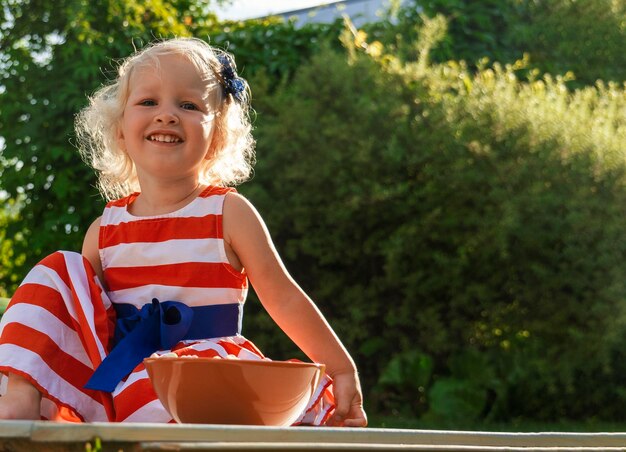 Foto uma menina muito encaracolada sentada no jardim com um prato de comida e olhando para a câmera