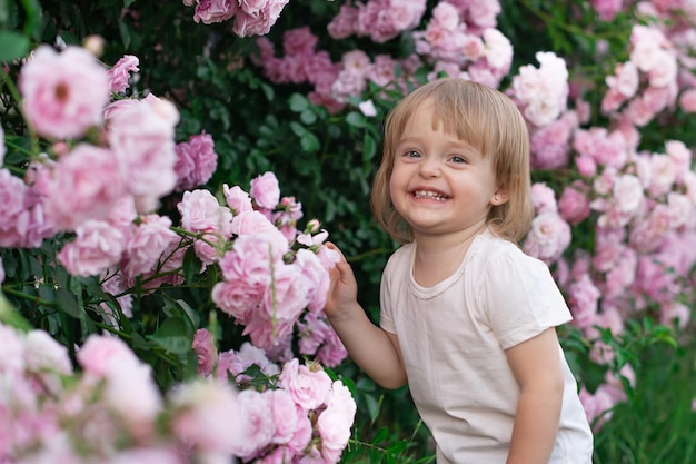 Uma menina no fundo de roseiras cor de rosa em um parque da cidade ri alegremente