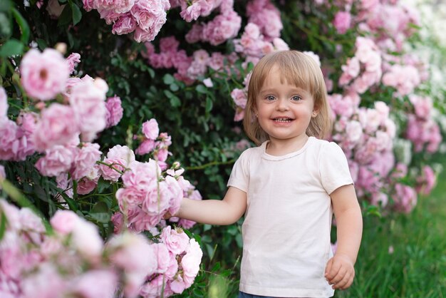 Uma menina no fundo de roseiras cor de rosa em um parque da cidade ri alegremente