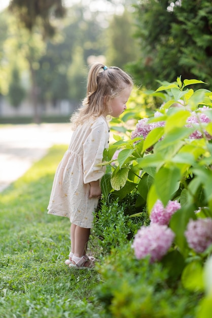 Uma menina no parque fareja um arbusto com uma flor curvada sobre ele