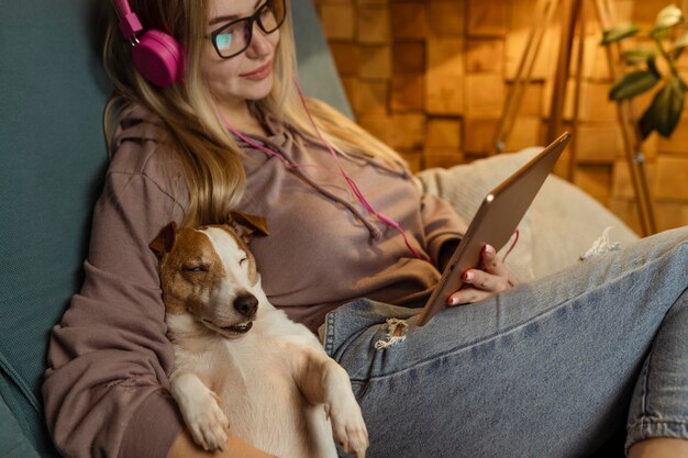 Foto uma menina no sofá deita-se com um cão em seu laptop e ouve música através de fones de ouvido freelancing e comunicação via internet