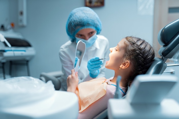 Uma menina paciente e uma dentista estão verificando os dentes no espelho após o tratamento no consultório odontológico