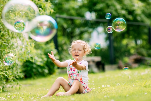 Uma menina pega bolhas de sabão no parque sentada na grama o conceito de um feliz