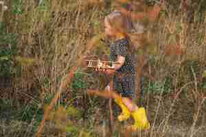 Foto uma menina pequena está brincando com um avião de madeira na natureza liberdade sonho imaginação conceito infância feliz uma menina bonita corre alegremente ao longo de um caminho na grama ri-se sorri