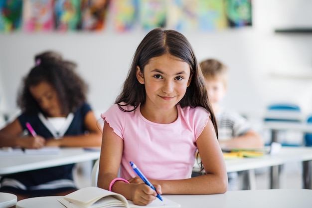 Uma menina pequena sentada na mesa na sala de aula olhando para a câmera