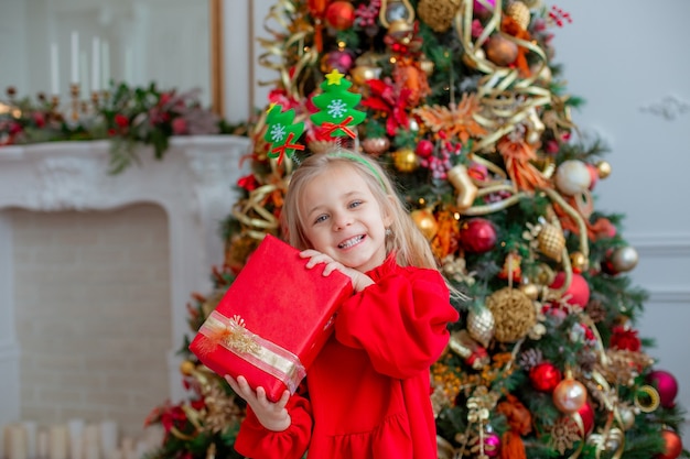 Uma menina perto da árvore de Natal guarda um presente em casa