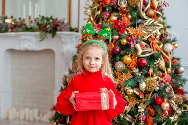 Uma menina perto da árvore de Natal guarda um presente em casa