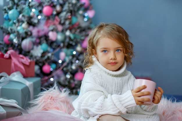 Uma menina perto da árvore de natal segura uma caneca de chá quente