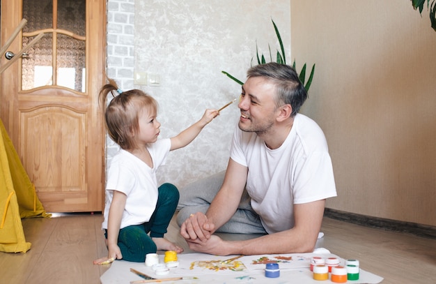 Uma menina pinta o rosto do pai com aquarela. jogos de família conjuntos