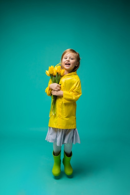 Uma menina pula em uma capa de chuva e botas de borracha com um buquê de tulipas amarelas em turquesa isolado